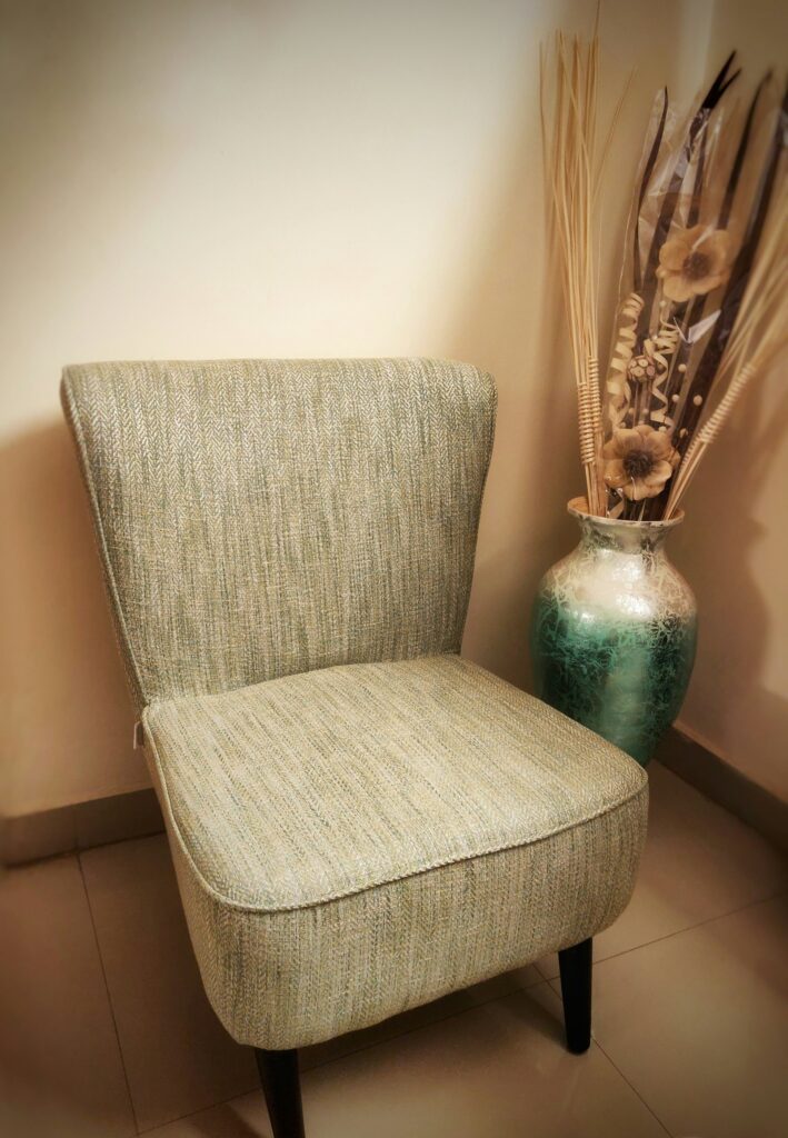 Upholstered armchair beside a vase of dried flowers